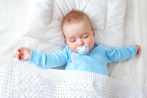 Seven month old baby sleeping on white blanket and pillow. Sleepy child on soft bedding with pacifier